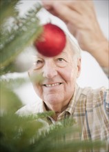 Portrait of senior man decorating Christmas tree. Photo : Jamie Grill Photography