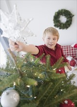 Boy (8-9) decorating Christmas tree. Photo : Jamie Grill Photography