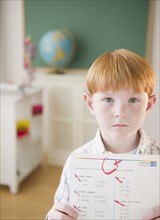 Portrait of boy (8-9) holding test results in classroom. Photo : Jamie Grill Photography