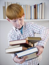 Boy (8-9) carrying stacked books. Photo : Jamie Grill Photography