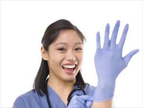 Young cheerful female surgeon putting on protective gloves. Photo : Dan Bannister