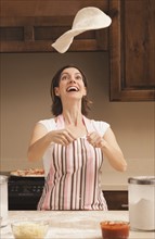 Woman tossing dough in kitchen. Photo : Mike Kemp