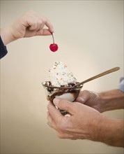 Close up of hands of grandfather and grandson (8-9) holding icecreame and cherry. Photo : Jamie