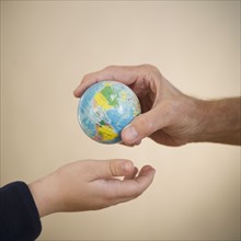 Close up of hands of grandfather and grandson (8-9) with small globe. Photo : Jamie Grill