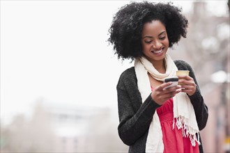USA, Washington State, Seattle, Cheerful young woman text messaging while holding takeaway coffee.