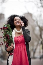 USA, Washington State, Seattle, Cheerful young woman holding christmas wreath while using mobile