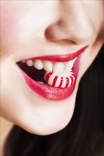 Close up of woman's mouths with red lipstick holding striped candy.