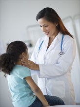 Female pediatrician examining girl (6-7) in doctor's office.