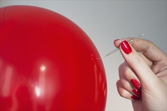 Close up of red balloon and woman's hand holding needle.