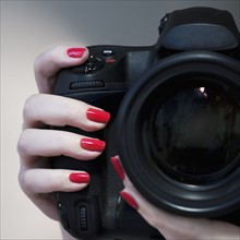 Close up of woman's hand with red nail polish holding camera.