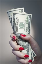 Close up of woman's hand with red nail polish holding bunch of dollar banknotes.