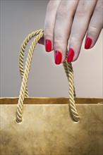 Close up of woman's hand with red nail polish holding string handle of paper bag.