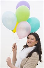 Young woman holding bunch of balloons smiling.