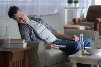 Man sitting on sofa, holding remote control and sleeping.