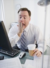 Businessman yawning in office. Photo: Jamie Grill Photography