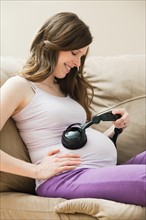 Young pregnant woman playing music through headphone to unborn baby. Photo: Mike Kemp