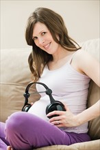Young pregnant woman playing music through headphone to unborn baby. Photo : Mike Kemp