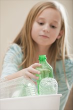 Studio shot of girl (8-9) placing plastic bottle in recycling bin. Photo: Mike Kemp