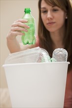Studio shot of woman (8-9) placing plastic bottle in recycling bin. Photo : Mike Kemp