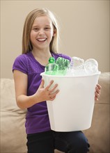 Portrait of girl (8-9) holding recycling bin with plastic bottles. Photo : Mike Kemp