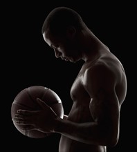 Studio shot of shirtless man holding basketball. Photo : Mike Kemp
