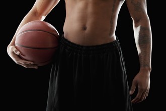 Studio shot of shirtless man holding basketball, mid section. Photo : Mike Kemp