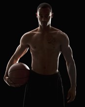 Studio portrait of shirtless man holding basketball. Photo : Mike Kemp