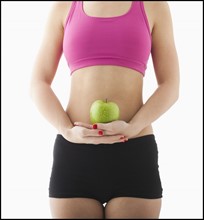 Young woman holding apple against belly. Photo: Mike Kemp
