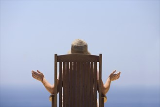 Rear view of woman sitting on wooden chair, facing sea. Photo: Justin Paget
