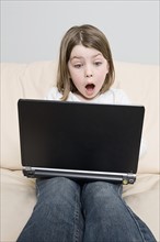Girl (6-7) with laptop sitting on sofa. Photo: Justin Paget