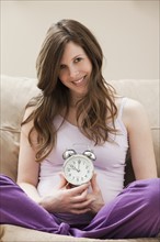 Young pregnant woman holding alarm clock. Photo: Mike Kemp