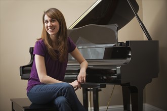 Young woman sitting by grand piano, smiling. Photo: Mike Kemp