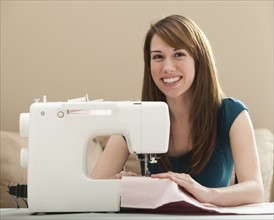Portrait of smiling young woman using sewing machine. Photo: Mike Kemp