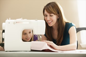 Girl (8-9) assisting young woman using sewing machine. Photo: Mike Kemp
