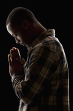 Studio shot of young man praying. Photo : Mike Kemp