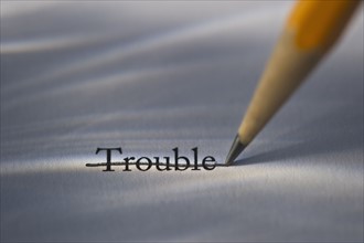 Studio shot of pencil crossing out the word trouble from piece of paper. Photo: Daniel Grill
