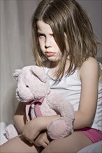 Studio portrait of sad girl (6-7) with pink teddy bear. Photo : Justin Paget