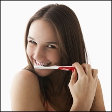 Studio portrait of young woman brushing teeth. Photo : Mike Kemp