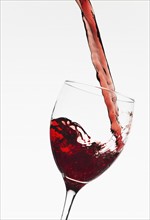 Close up of red wine being poured into glass on white background.