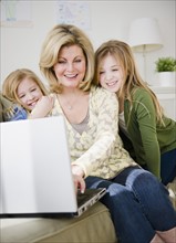 Mother and daughters (8-11) using laptop. Photo : Jamie Grill Photography