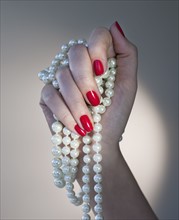 Close up of woman's hands with red nail polish holding pearls.