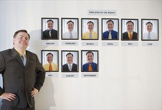 Businessman standing in front of employee of the month portraits. Photo : Jamie Grill Photography