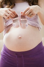 Young pregnant woman showing two female baby shoes. Photo : Mike Kemp