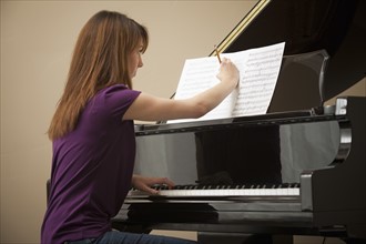 Young woman marking score before setting to play grand piano. Photo : Mike Kemp