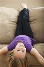 Portrait of girl (8-9) lying on sofa. Photo : Mike Kemp