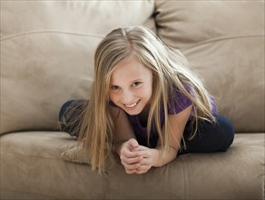 Portrait of girl (8-9) sitting on sofa. Photo : Mike Kemp