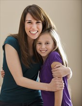 Studio portrait of young woman hugging sister (8-9). Photo : Mike Kemp