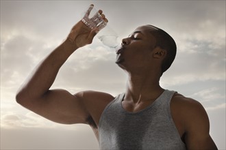Athlete young man drinking water form bottle, cloudy sky in background. Photo : Mike Kemp