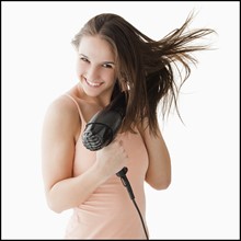 Studio portrait of young woman blow drying hair. Photo: Mike Kemp