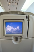 Airplane seat with monitor displaying clouds. Photo : Tetra Images